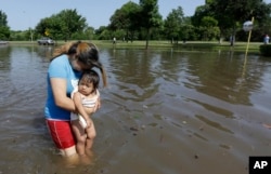 Phụ nữ bồng con qua khu vực ngập nước ở Houston, Texas, ngày 26/5/2015.